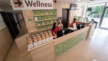 A reception desk with a sign indicating the wellness area. There are receptionists behind the desk, and a menu board is visible.