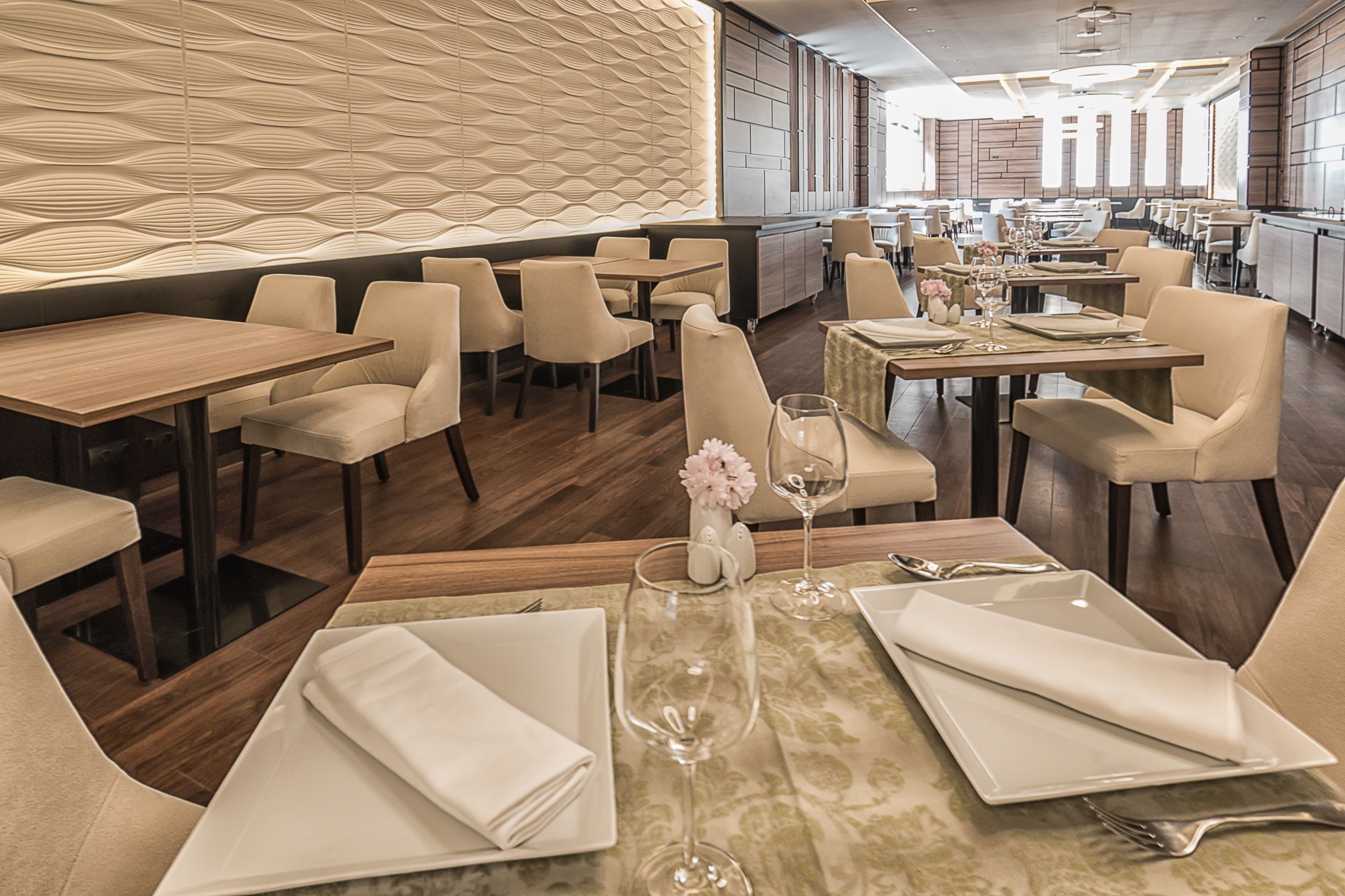 A modern restaurant interior with a patterned wall, wooden tables, and comfortable seating.