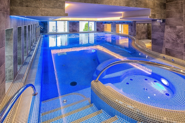 Una amplia piscina interior con un jacuzzi, paredes de azulejos y vistas despejadas al exterior.