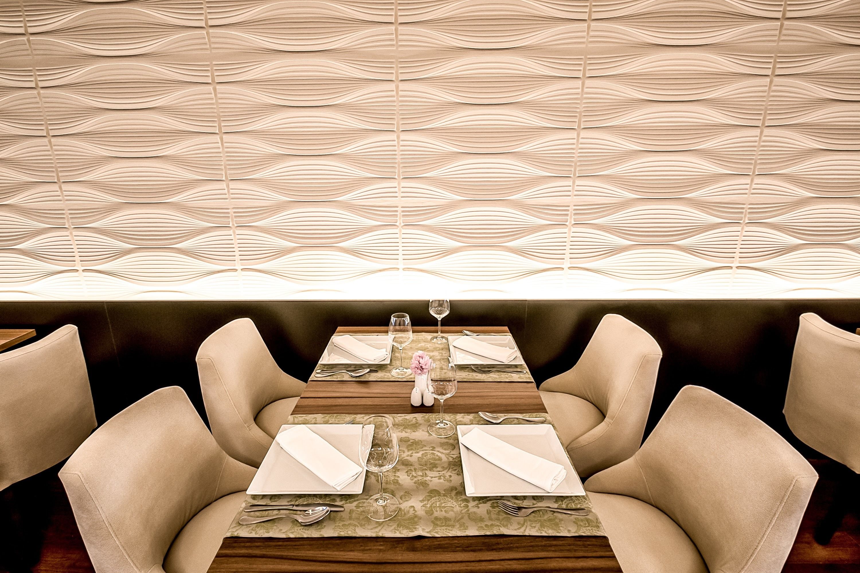 Un comedor con una pared estampada, una mesa de madera con servilletas blancas y sillas tapizadas en color beige.
