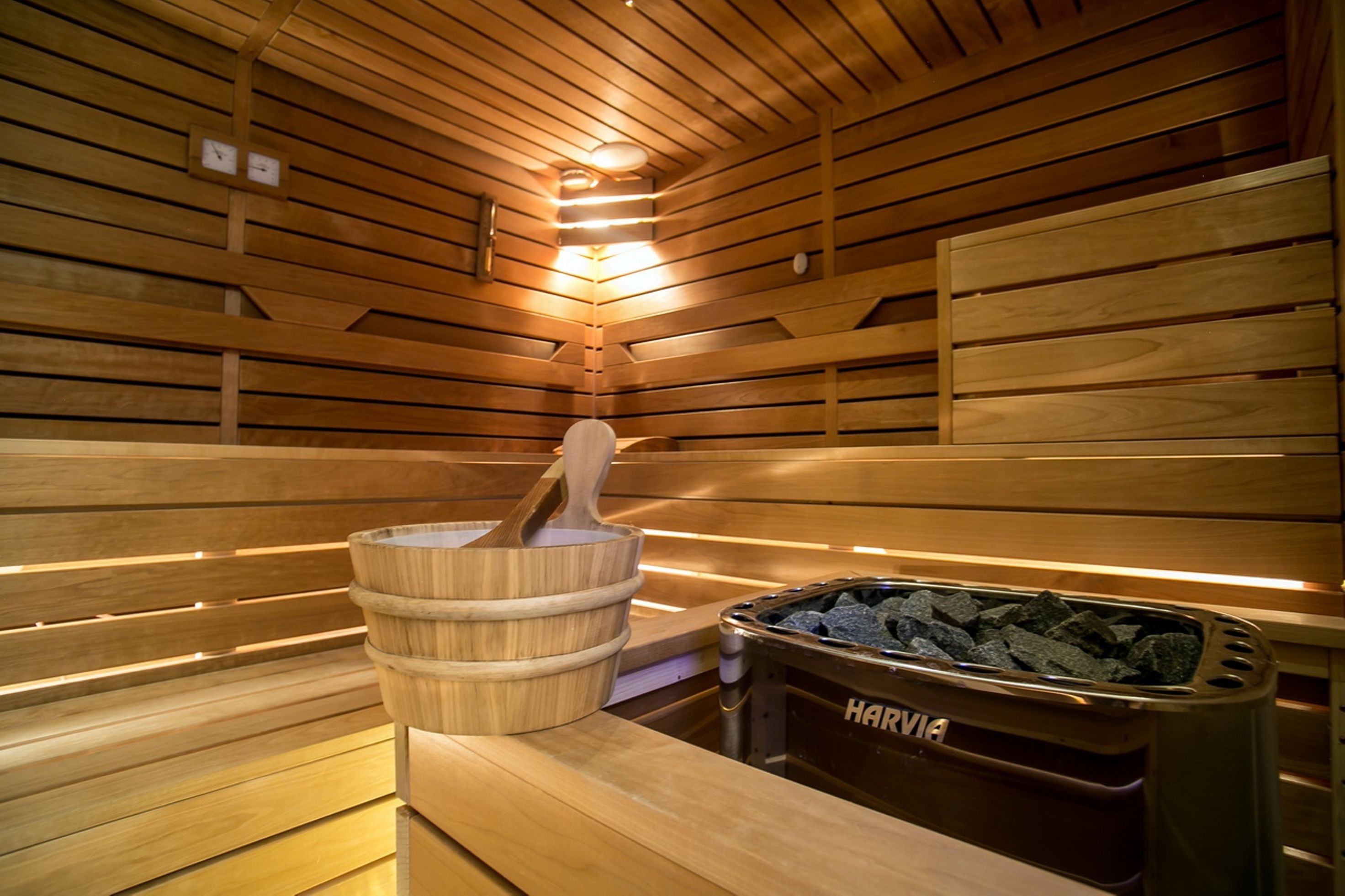 A sauna with wooden benches, a wooden bucket with a mallet, and a container labeled "HARVIA" for stones.