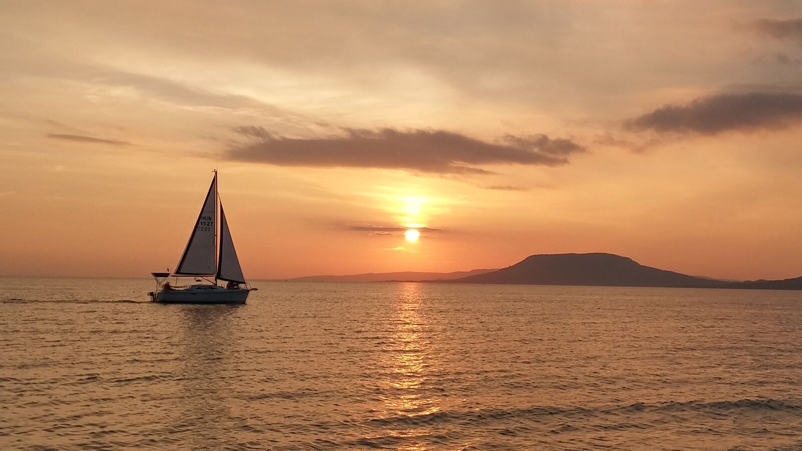 Un velero en aguas tranquilas durante el atardecer, con una montaña distante y un cielo despejado.
