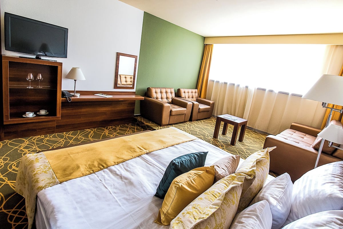 Ein Hotelzimmer mit einem Bett, zwei Sesseln, einem kleinen Tisch, einem Fernseher und einer Minibar.