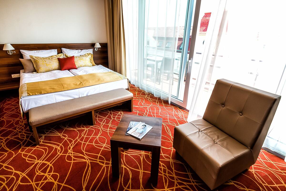 Ein Hotelzimmer mit Bett, einer Bank, einem Sessel und einem kleinen Tisch mit einer Zeitschrift.