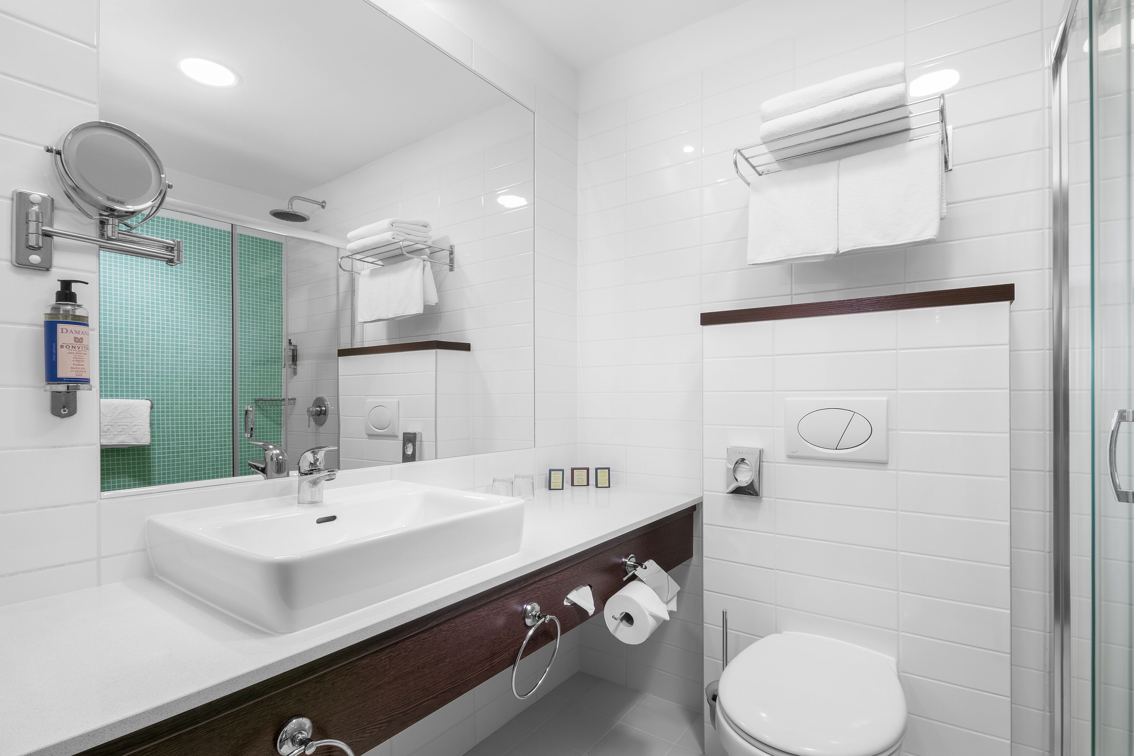 Un baño moderno con un espejo grande, lavamanos blanco y cabina de ducha de vidrio.