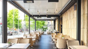 Ein Straßencafé mit Korbtischen und -stühlen, großen Fenstern und Blick auf die Straße.