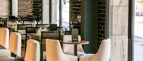 A modern restaurant interior with white chairs, round tables, and a brick wall.