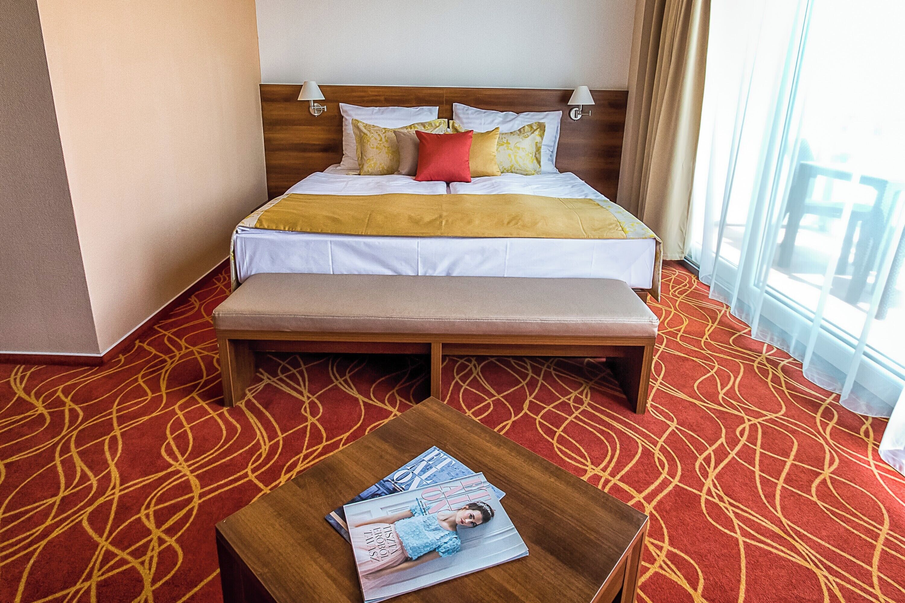 A hotel room with a large bed, a bench, and a table with magazines.