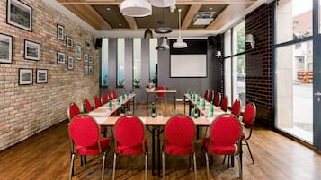 Ein Konferenzraum mit langem Tisch, roten Stühlen und gerahmten Bildern an der Ziegelwand.