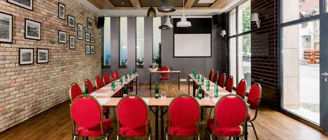 Un salón de conferencias con una larga mesa, sillas rojas y cuadros en la pared de ladrillo.
