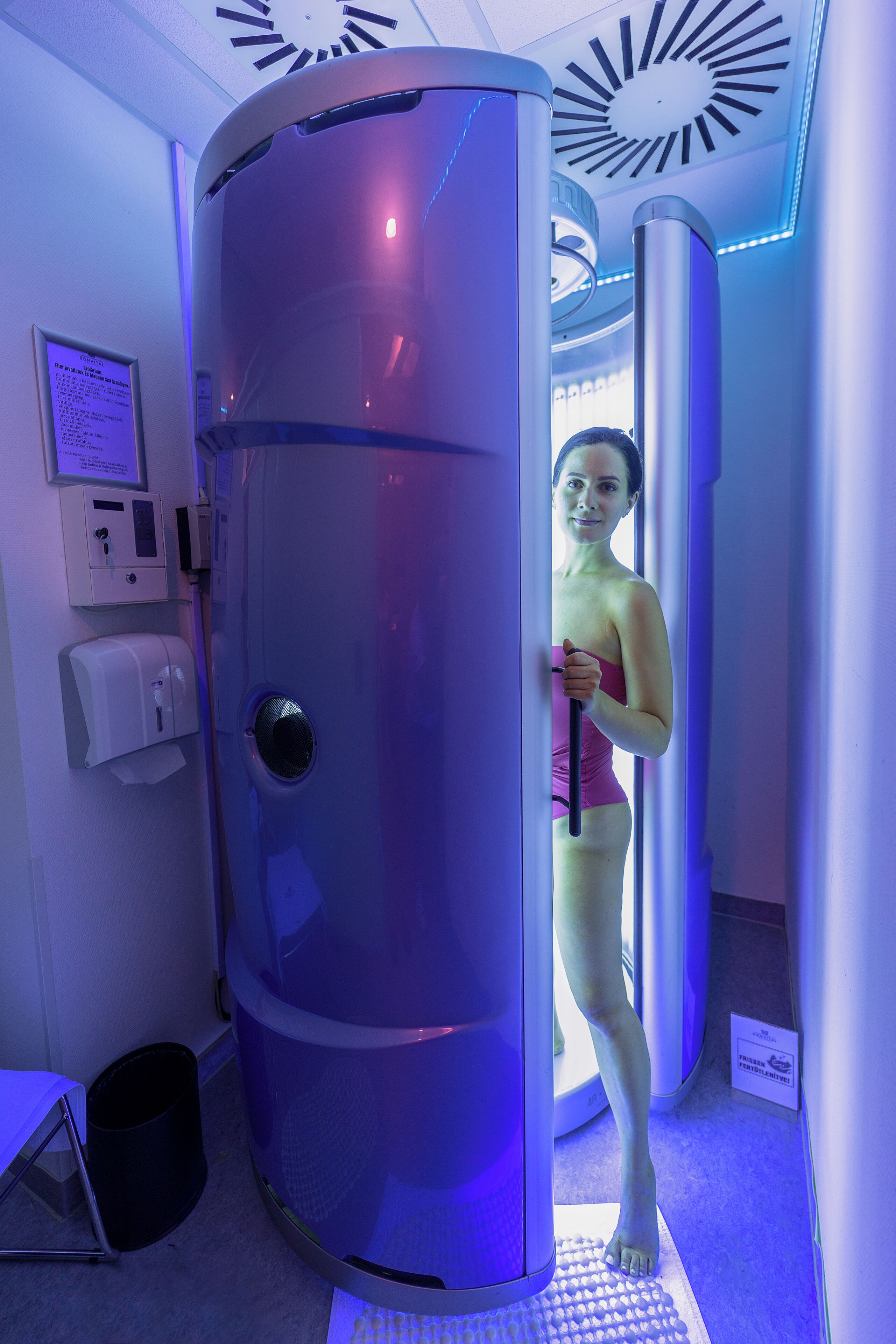 A spa room with a large cylindrical machine, a hand sanitizer dispenser, and a small trash bin.