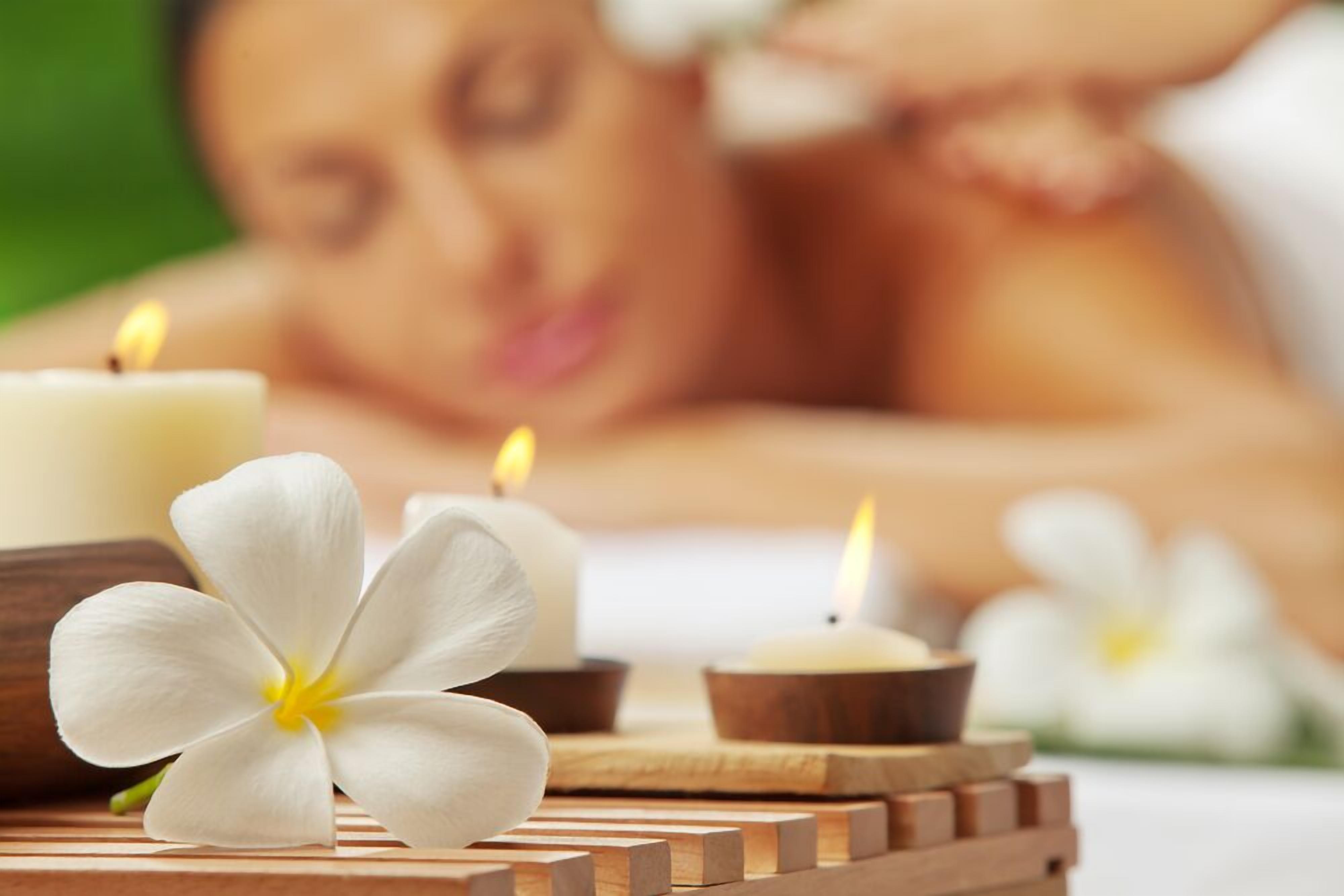 A spa setting with candles and flowers on a wooden tray.