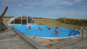 Una piscina exterior con cubierta de madera, barandillas de seguridad metálicas y un cielo azul despejado.