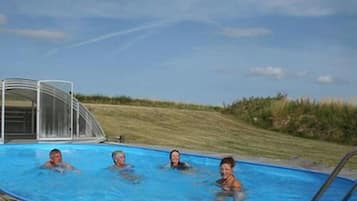 Piscina com céu azul e área gramada ao fundo.