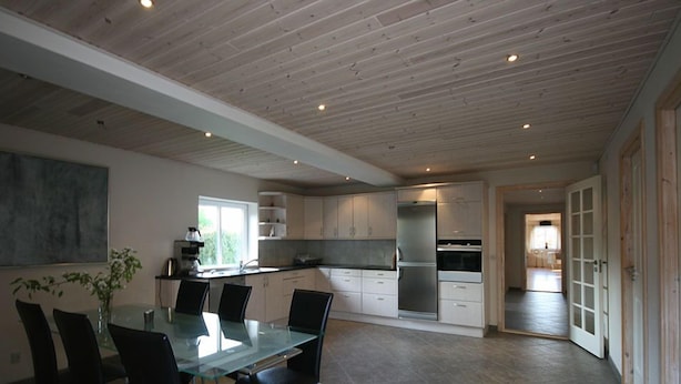 Una cocina moderna con armarios blancos, un refrigerador de acero inoxidable y una mesa de comedor de vidrio con sillas.