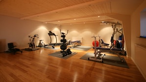 Un gimnasio amplio con pisos de madera, diversos equipos de ejercicio y colchonetas.