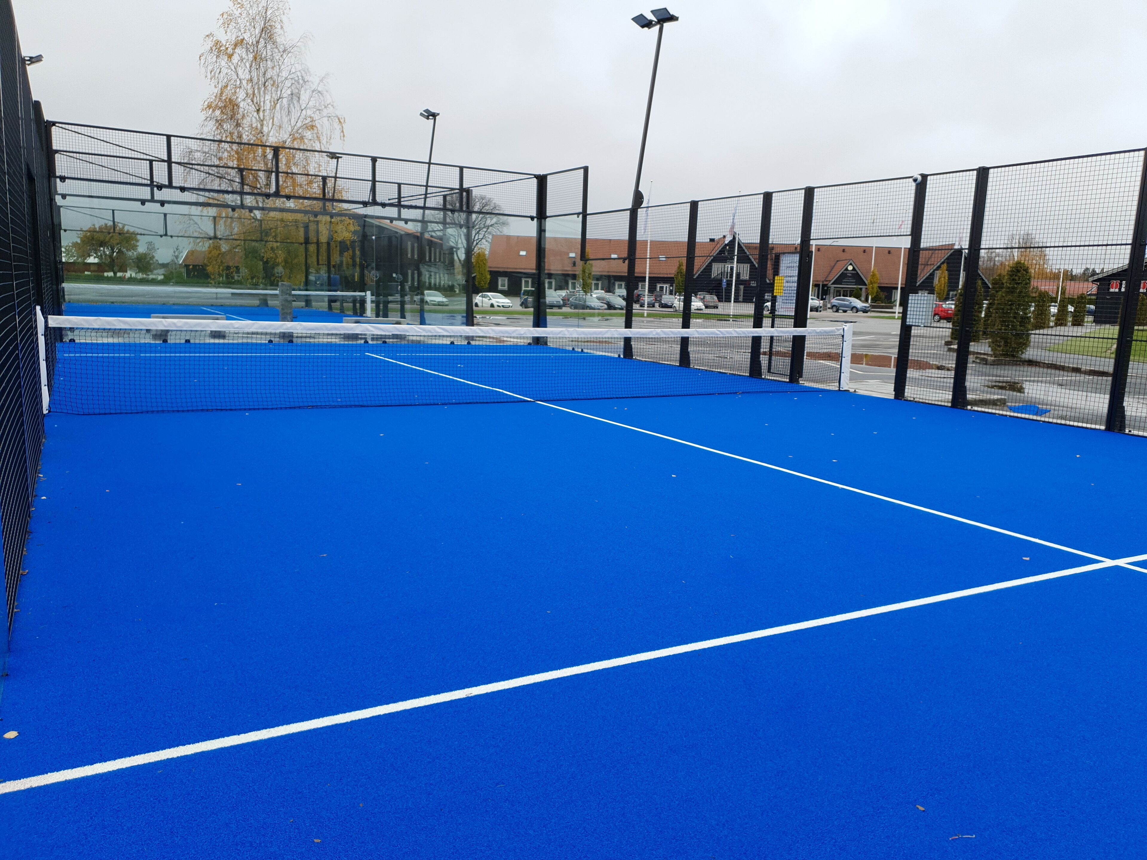 Una cancha de tenis con superficie azul y líneas blancas delimitadoras, rodeada por una cerca negra.