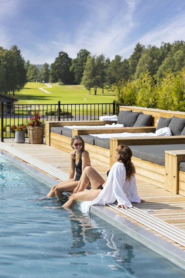 A poolside area with wooden deck seating and a view of a golf course. - Lannalodge (Vintrosa)