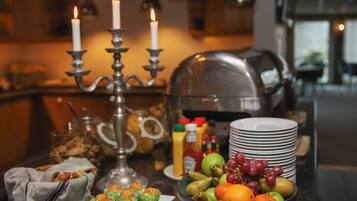 A buffet setup with a variety of food items, including fruits, pastries, and condiments, arranged on a table with a candelabra and plates stacked in the background.