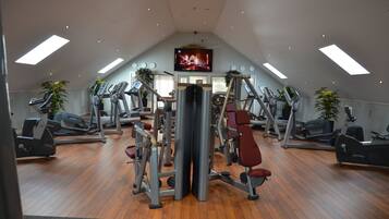 A gym with various exercise machines, a TV screen, and wooden flooring.