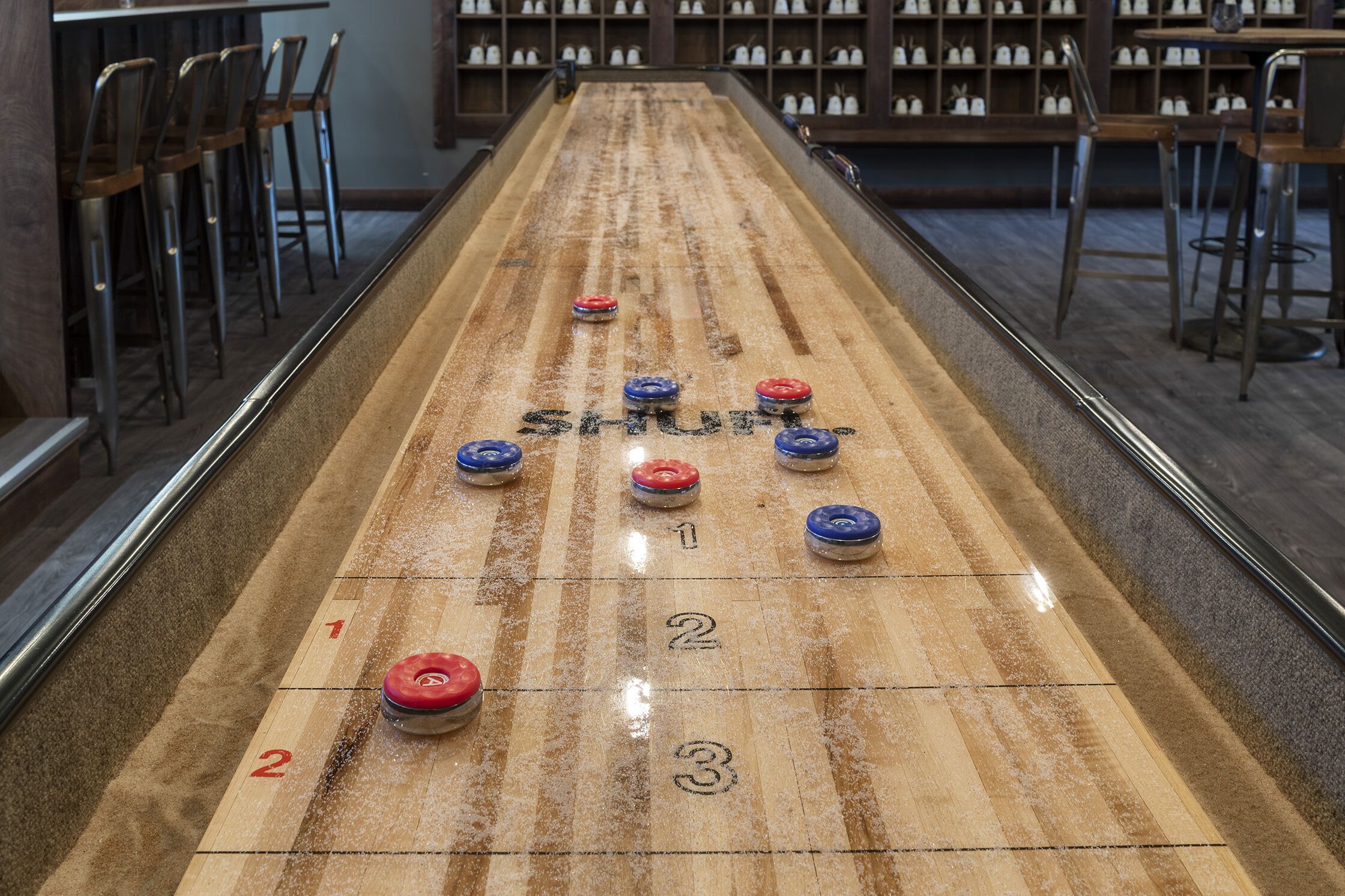 Ett shuffleboard-bord med numrerade områden för poängräkning och puckar i rött, blått och vitt.