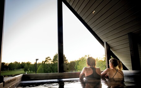 Two people in a hot tub with a view of trees and a clear sky.