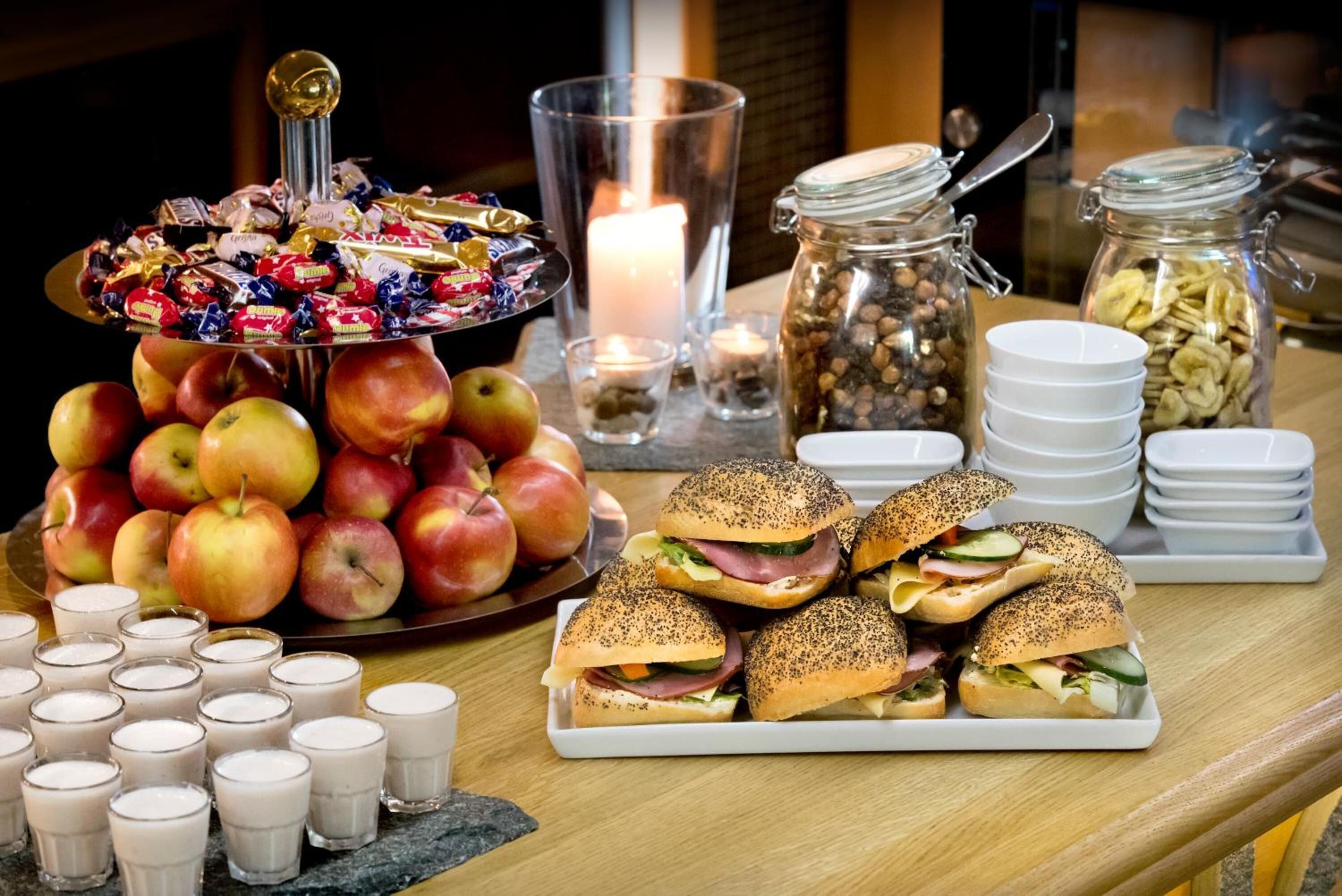 A buffet table with a variety of food items including apples, sandwiches, and milkshakes.