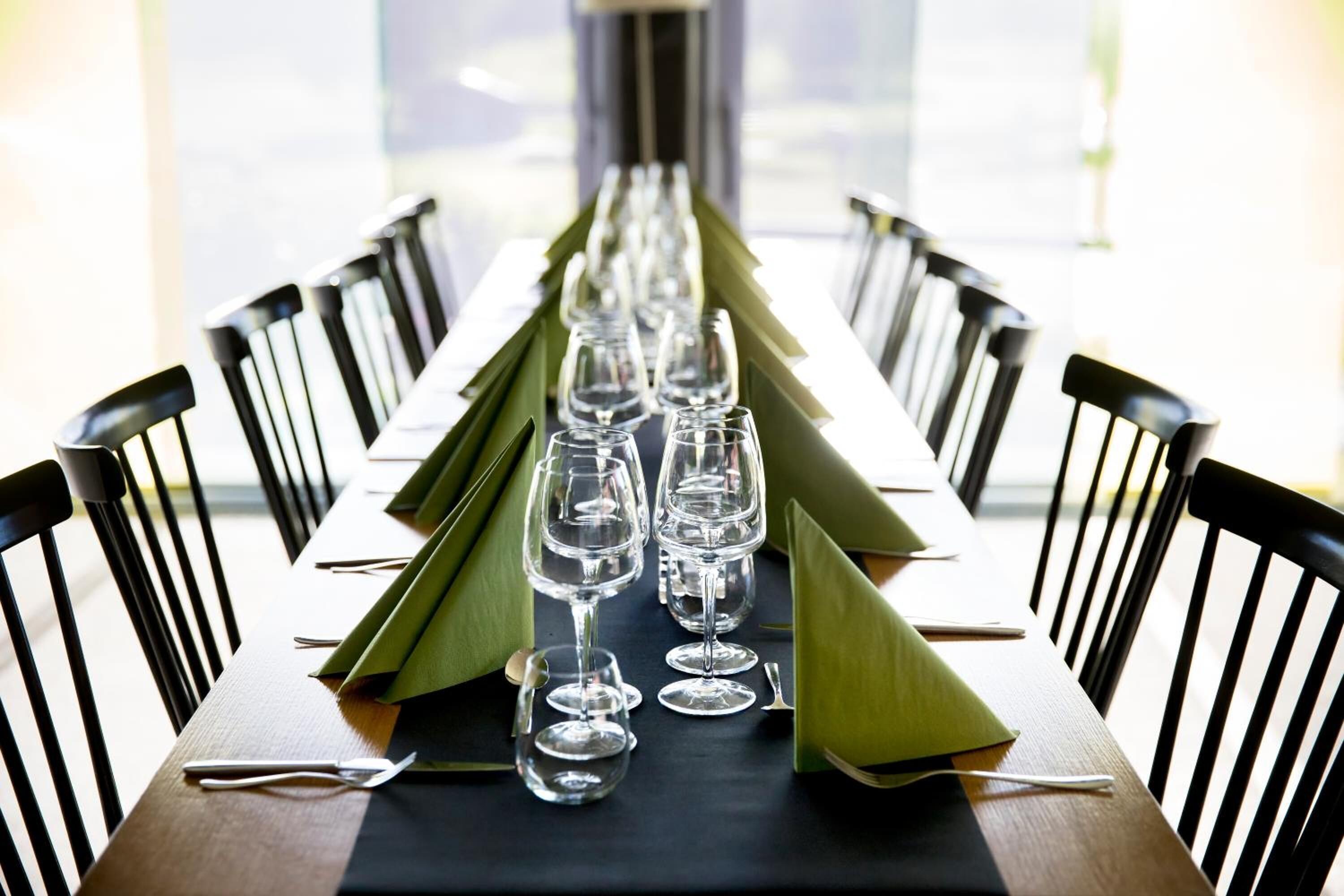 Een eettafel gedekt met verschillende wijnglazen en groene servetten, omringd door zwarte stoelen.