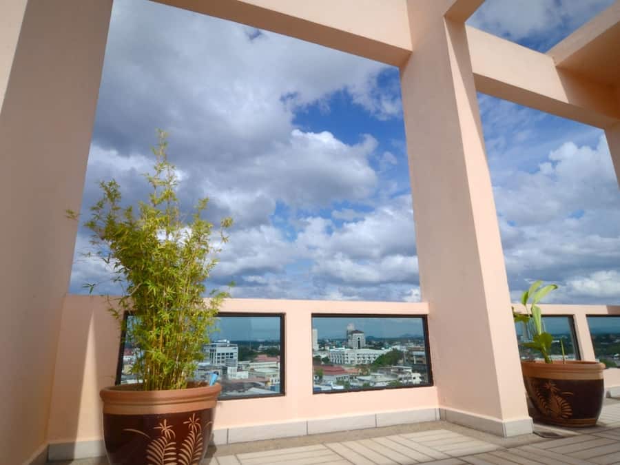 A balcony with large windows overlooking a cityscape, potted plants, and a clear sky.