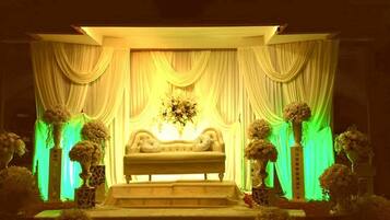 A stage with a sofa and draped curtains, flanked by flower arrangements.
