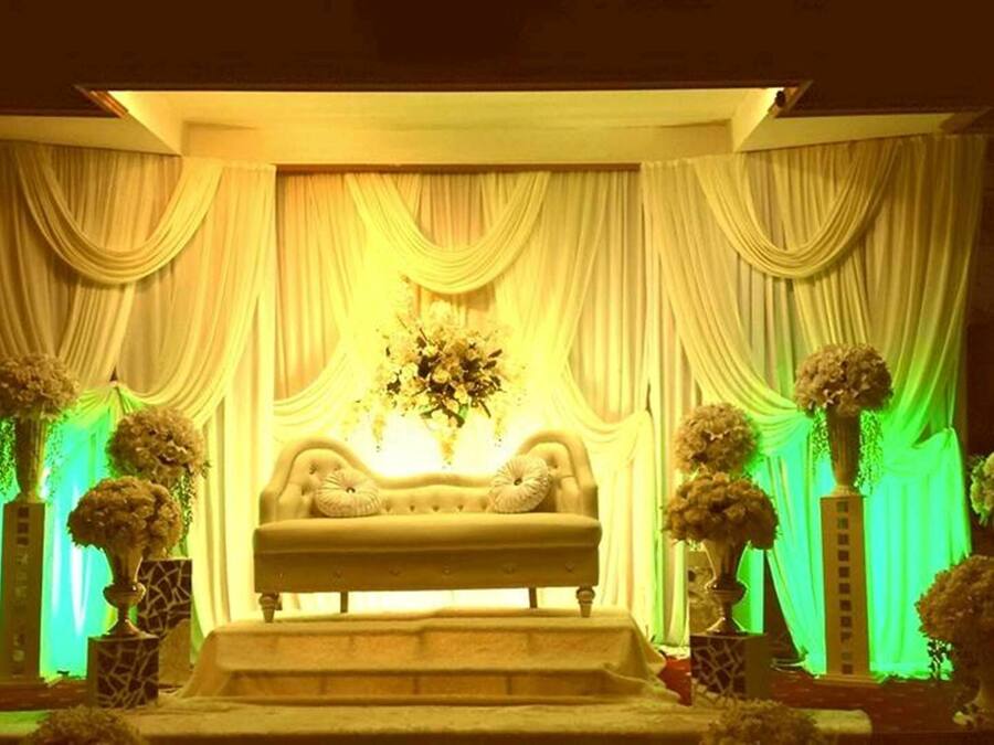 A stage with a sofa and draped curtains, flanked by flower arrangements.