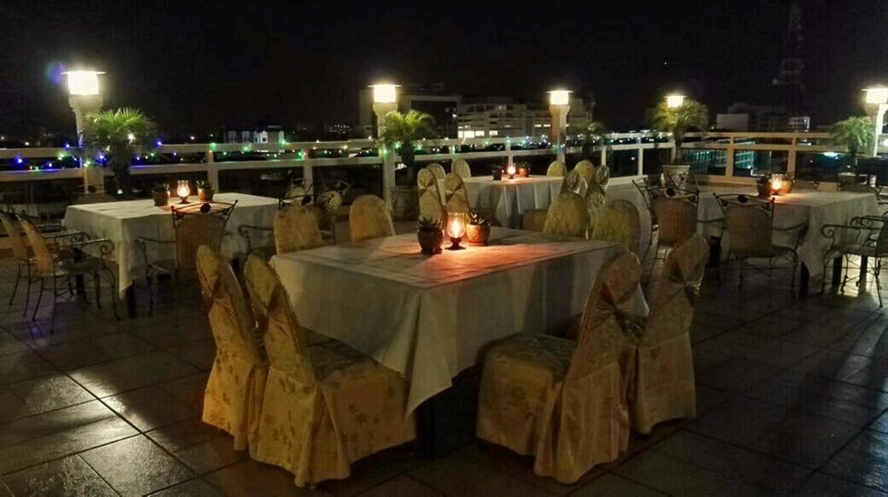 An outdoor dining area with tables and chairs, illuminated by ambient lighting.
