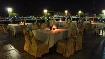 An outdoor dining area with tables and chairs, illuminated by ambient lighting.