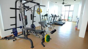 Un gimnasio con equipo de levantamiento de pesas, cintas de correr y una banca.