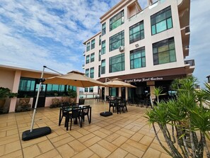 An outdoor patio area with tables and chairs, umbrellas, and potted plants. - Crystal Lodge (Kota Bharu)