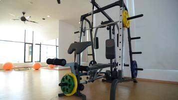 A gym with a weightlifting station, exercise balls, and large windows.