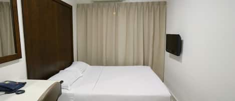 A hotel room with a bed, a desk with a telephone, a wall-mounted air conditioner, and a curtain.
