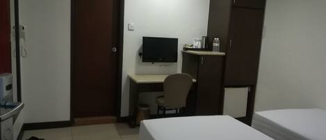 Habitación de hotel con cama, escritorio y silla, televisor, armario y una pequeña kitchenette.