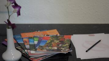 A collection of travel brochures, a pen, and a white vase with purple flowers on a table.