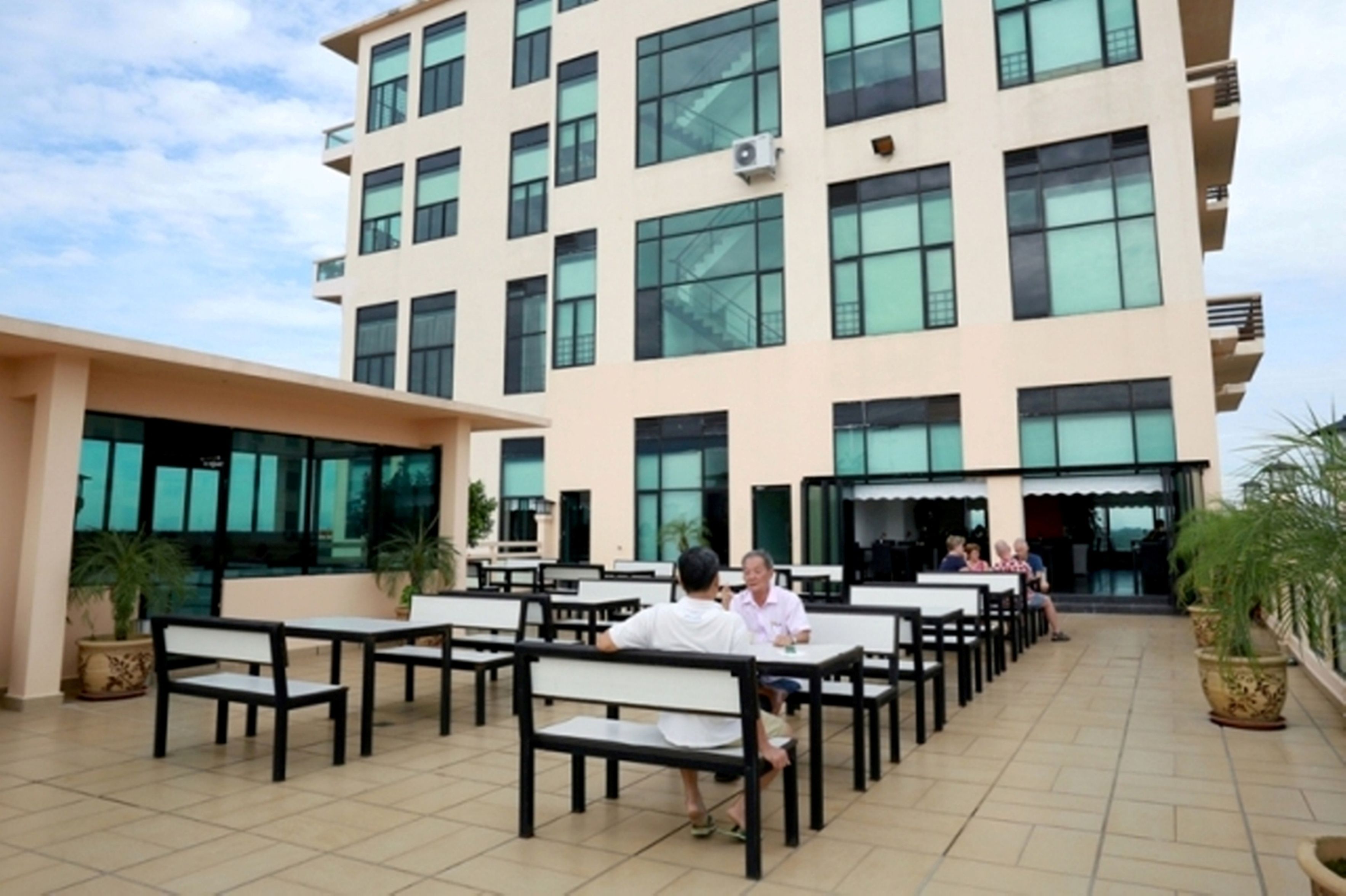 A modern building with multiple floors, large windows, and outdoor seating areas with tables and chairs.