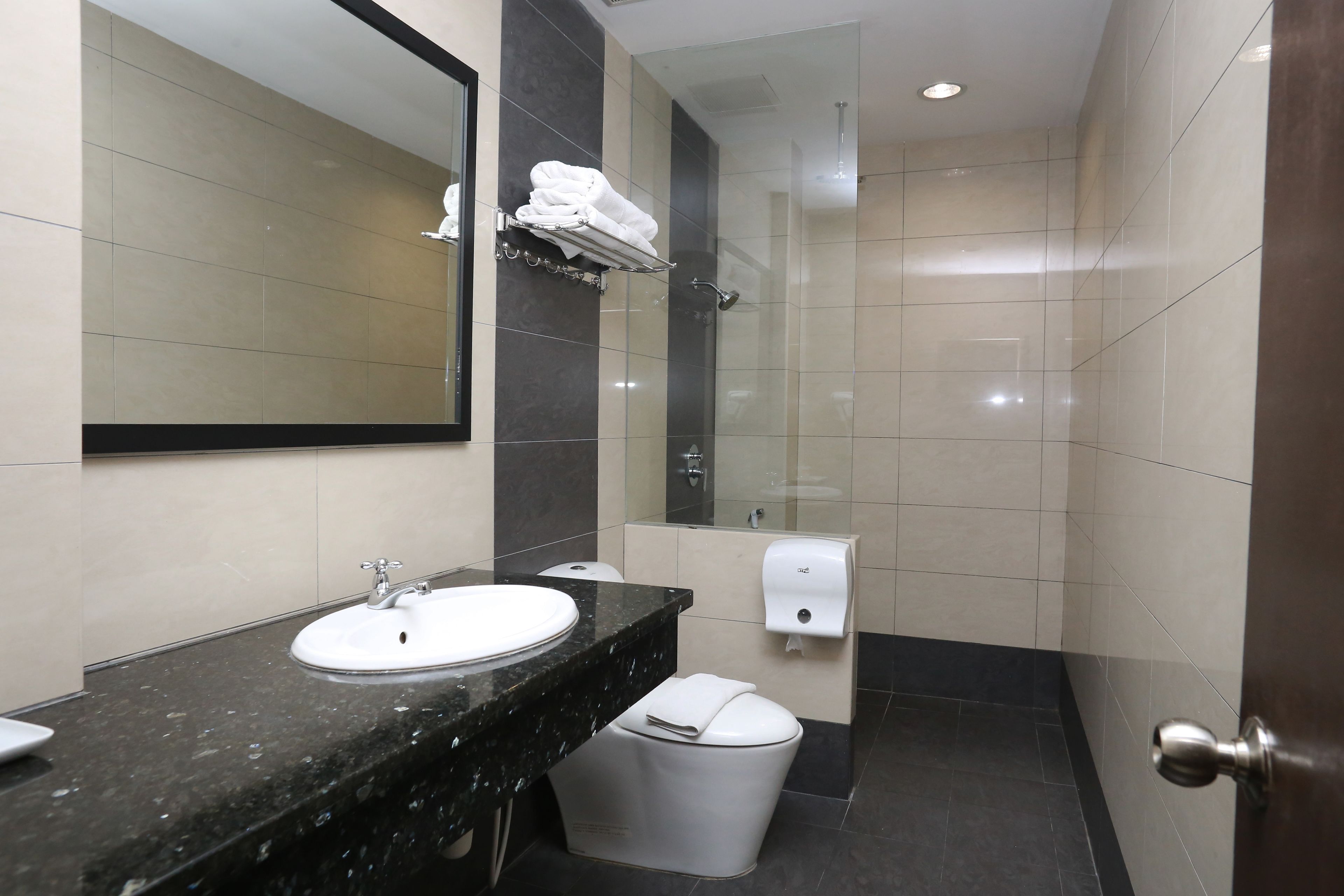 Un baño moderno con lavamanos, espejo, toallero, ducha e inodoro.