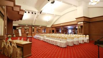 A large hall with rows of tables and chairs, a stage, and a piano.
