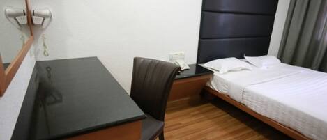 Une chambre d’hôtel avec un bureau en bois, une chaise, un lit avec une literie blanche et une tête de lit noire.