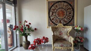 A room with a large zodiac wall art, a floral armchair, and multiple flower arrangements. - Rongkhem-City Hotel (Rong Kwang)