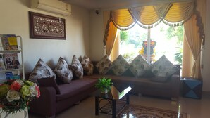 A living room with a sofa, decorative pillows, a small table with a plant, a framed picture on the wall, and a window with curtains. - Rongkhem-City Hotel (Rong Kwang)