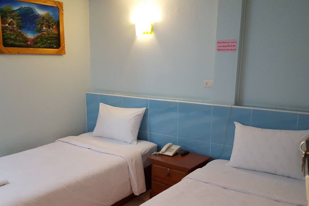 A hotel room with two beds, a nightstand with a phone, a painting on the wall, and a sign indicating the room number.