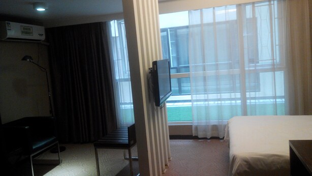 A hotel room with a bed, a desk, a chair, a television, and a window with curtains. - Jiashiting Hotel Hankou Railway Station (Wuhan)