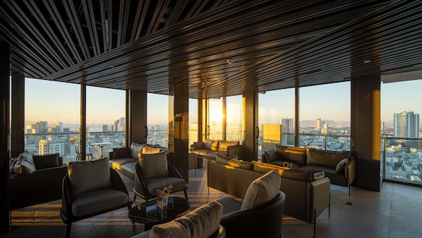 A spacious lounge area with multiple seating options and large windows offering a city view. - Luxtery Hotel (Da Nang)
