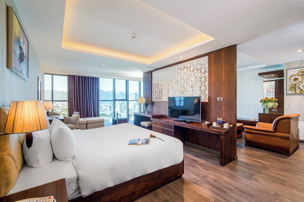 A modern hotel room with a large bed, a TV, a desk, and a seating area.