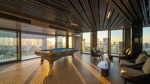 A pool table in a modern lounge area with large windows offering city views. - Luxtery Hotel (Da Nang)